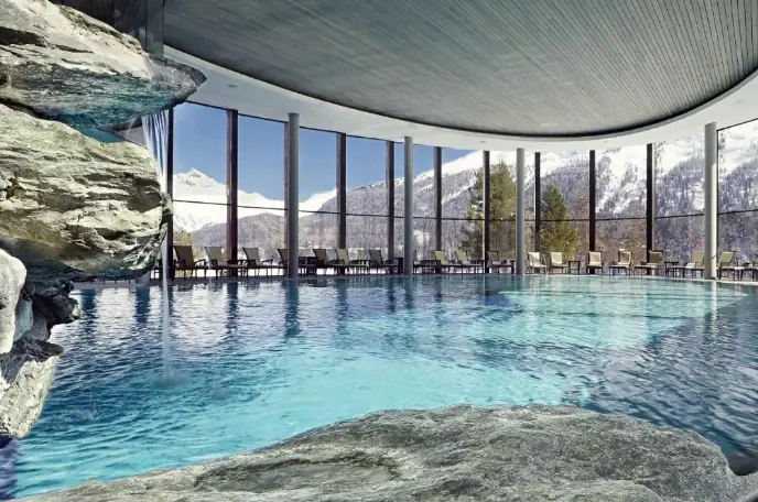 Innenpool mit Felswand und raumhoher Fensterfront zur verschneiten Bergwelt