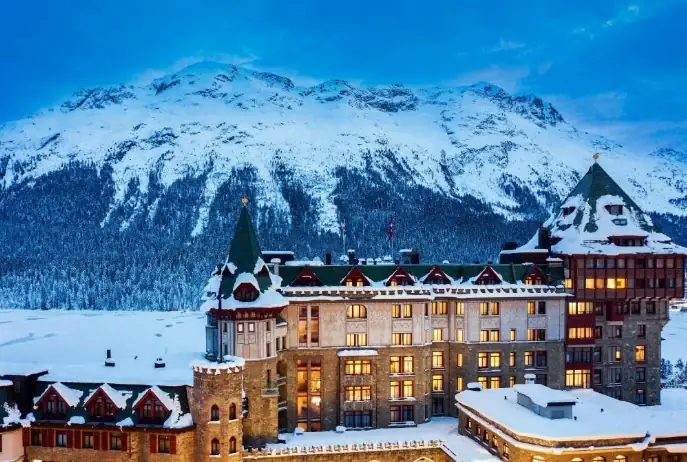 Badrutt’s Palace im Winter, beleuchtet vor der verschneiten Bergkulisse von St. Moritz