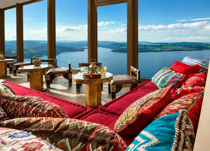 Lounge con cojines de colores y detalles orientales ante ventanales panorámicos hacia el lago