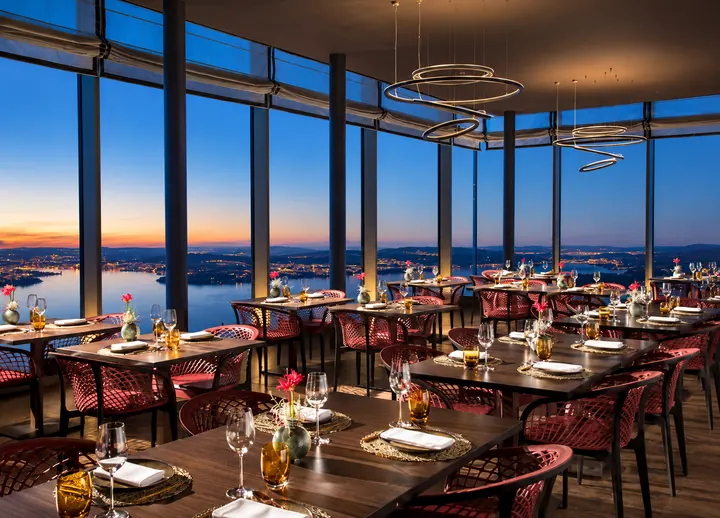 Restaurante con ventanales panorámicos y vista sobre el lago y las montañas al anochecer
