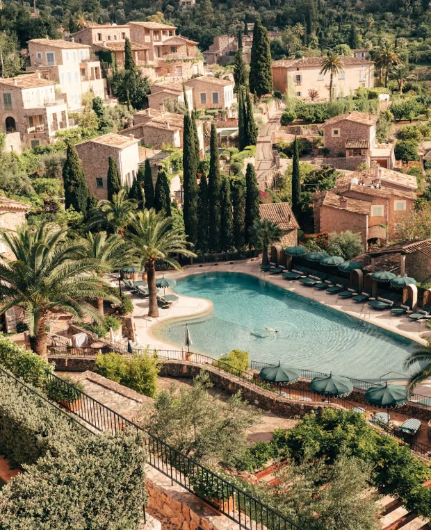 La Residencia in Deià: Poolanlage zwischen Palmen und Zypressen, dahinter die Natursteinhäuser des Dorfes