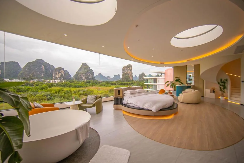 Suite mit rundem, auf die Berge ausgerichtetem Bett, ovalen Oberlichtern und freistehender Wanne vor Panoramafenstern.