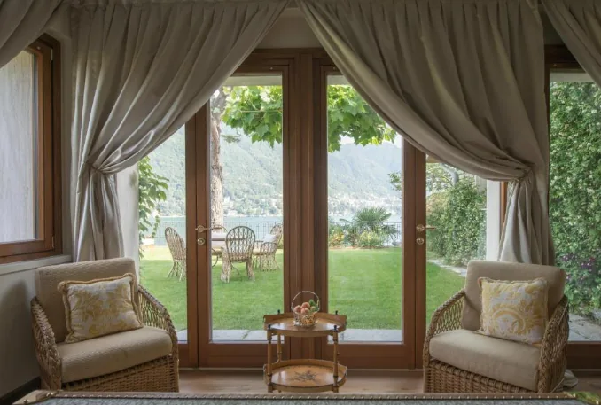 Wohnraum der Casa al Lago mit Korbsesseln und Blick durch Terrassentüren auf den Comer See