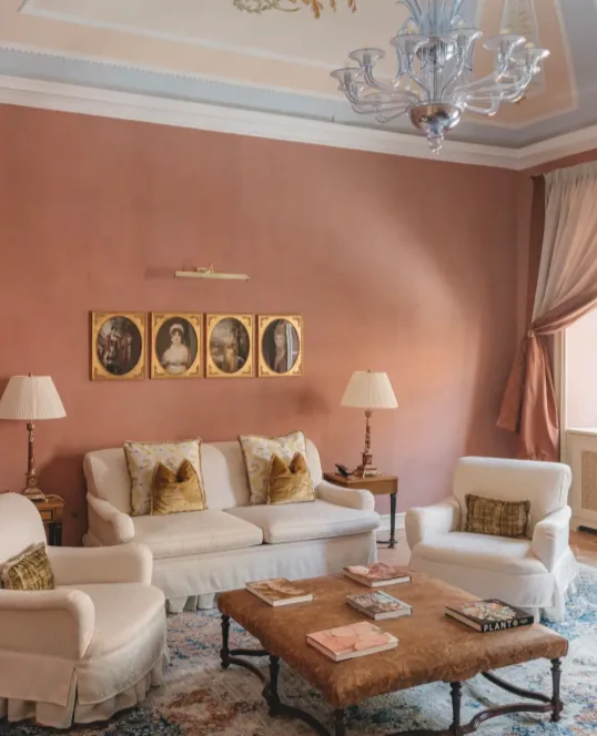 Rosafarbener Salon mit weißen Sofas, Murano-Leuchter und antiken Porträts